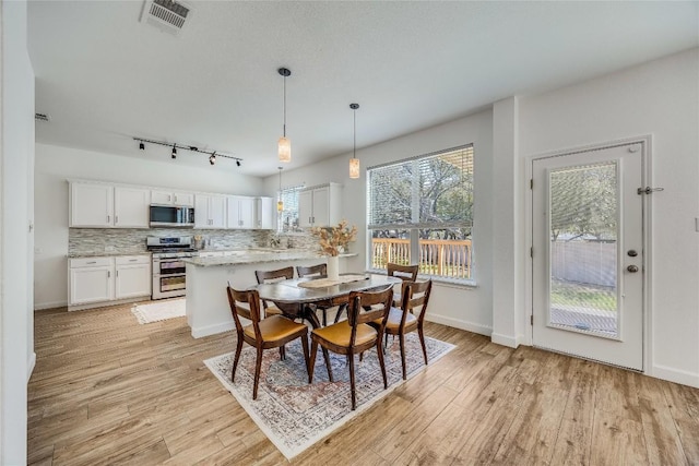 dining space with visible vents, baseboards, light wood-style floors, and rail lighting