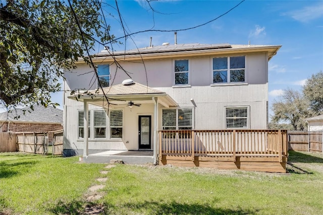 back of property featuring solar panels, a fenced backyard, ceiling fan, a deck, and a lawn