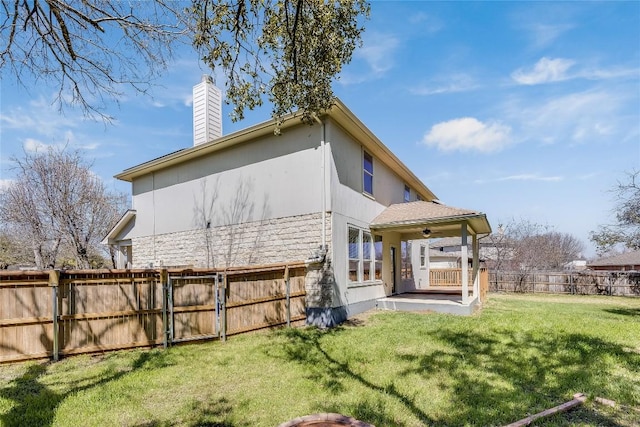 rear view of property featuring a yard, a fenced backyard, a chimney, and stucco siding