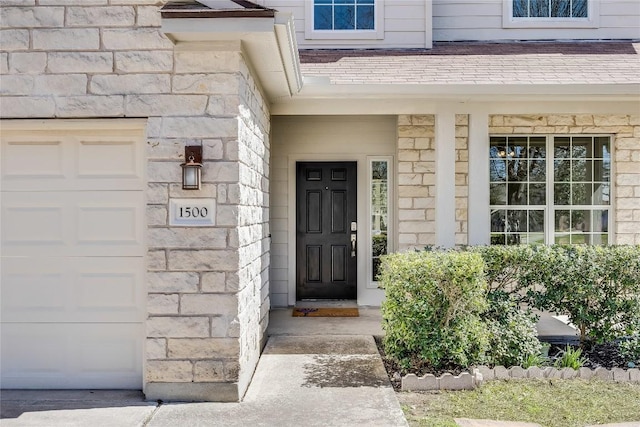 view of exterior entry with stone siding, an attached garage, and a shingled roof