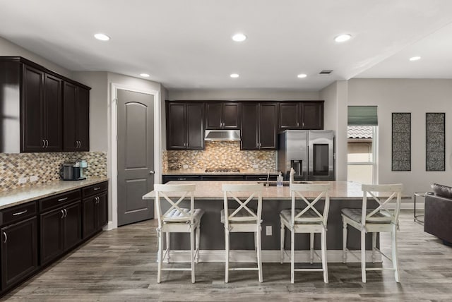 kitchen with under cabinet range hood, a kitchen breakfast bar, wood finished floors, and appliances with stainless steel finishes