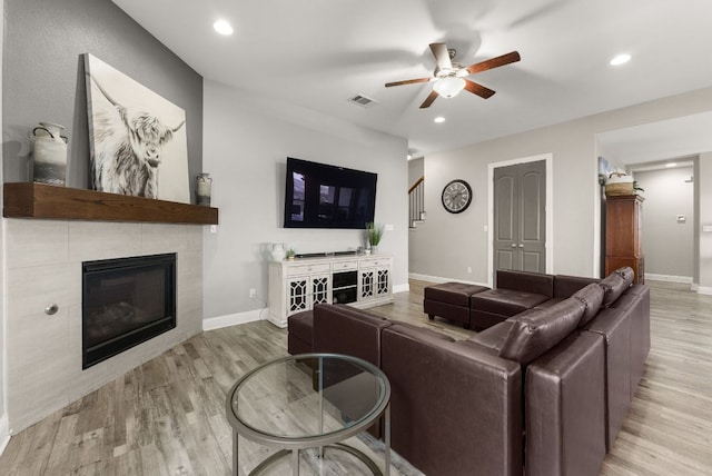 living area with a tiled fireplace, stairway, baseboards, and wood finished floors