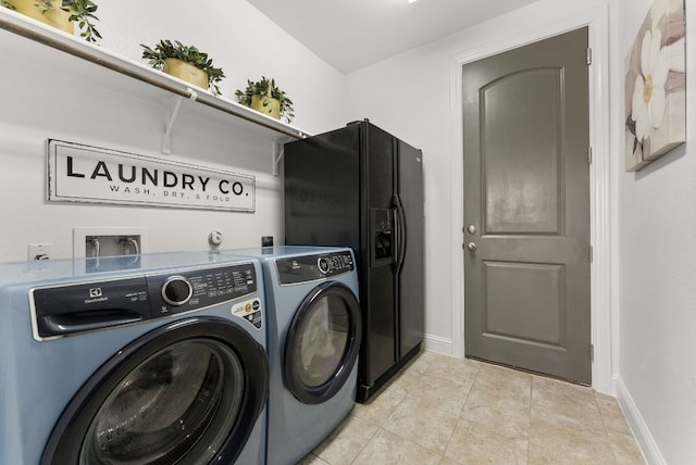 washroom with baseboards, light tile patterned flooring, laundry area, and washing machine and clothes dryer