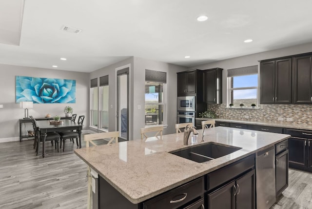 kitchen with visible vents, a kitchen island with sink, stainless steel appliances, a sink, and tasteful backsplash