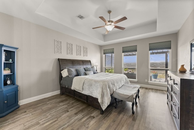 bedroom with a tray ceiling, multiple windows, wood finished floors, and baseboards