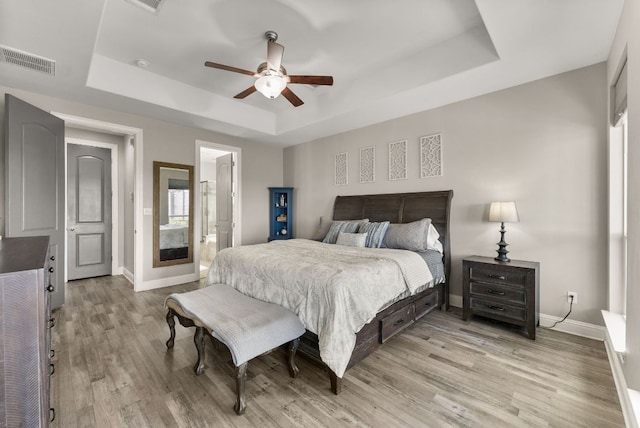 bedroom with a raised ceiling, light wood-style floors, visible vents, and baseboards