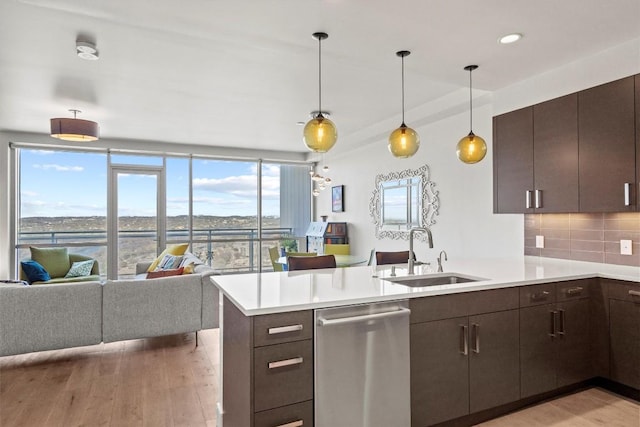 kitchen featuring tasteful backsplash, dishwasher, light wood-type flooring, a peninsula, and a sink