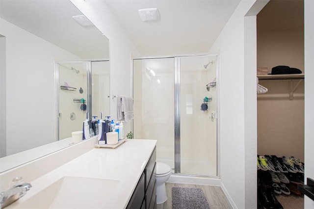 bathroom with vanity, wood finished floors, a stall shower, a spacious closet, and toilet