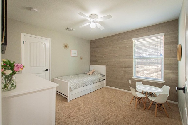 bedroom with wooden walls, multiple windows, light colored carpet, and visible vents