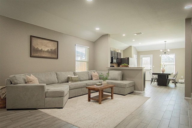 living area featuring a wealth of natural light, light wood-type flooring, visible vents, and vaulted ceiling