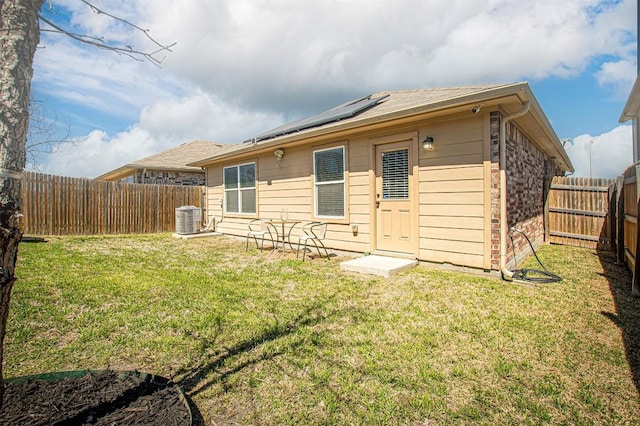 rear view of house with solar panels, central air condition unit, a yard, and a fenced backyard