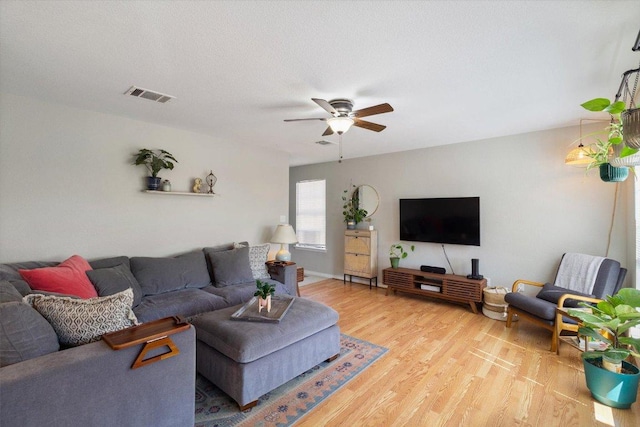 living room featuring light wood-style flooring, a ceiling fan, visible vents, and a textured ceiling