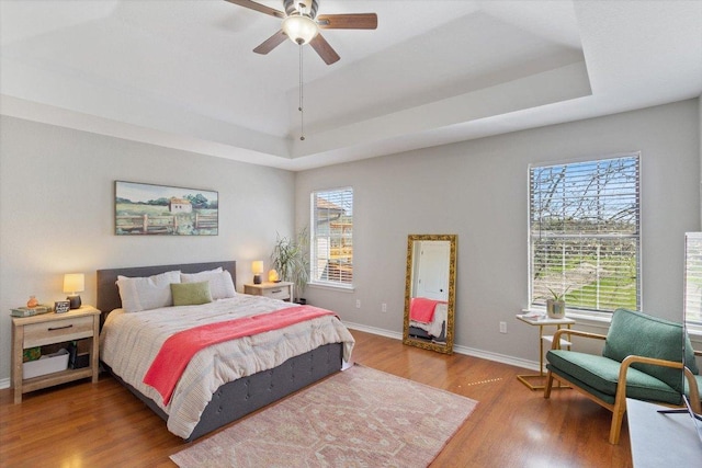 bedroom with multiple windows, a raised ceiling, baseboards, and wood finished floors