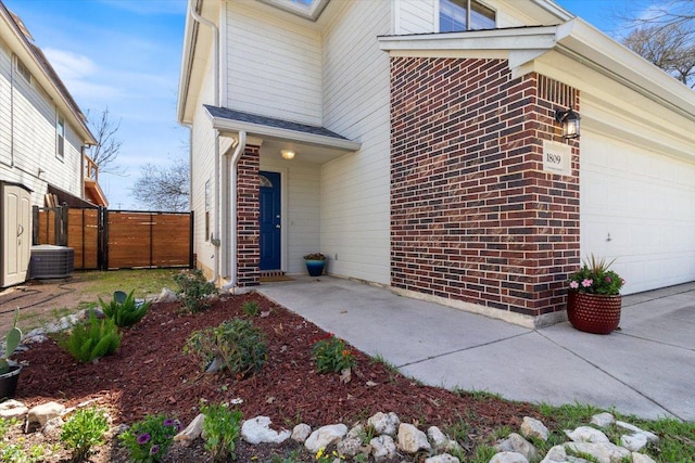 entrance to property with a gate, fence, a garage, brick siding, and central AC unit