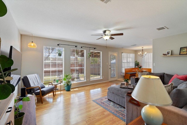 living room with ceiling fan with notable chandelier, wood finished floors, visible vents, and a textured ceiling