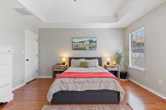 bedroom featuring baseboards, a tray ceiling, and wood finished floors