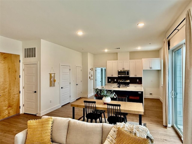 kitchen with light wood-type flooring, visible vents, an island with sink, stainless steel appliances, and white cabinets