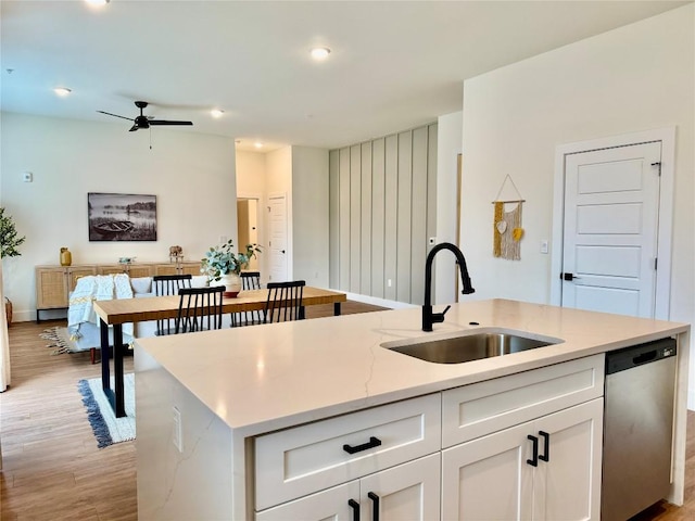 kitchen featuring a sink, dishwasher, light wood-style flooring, white cabinets, and a kitchen island with sink