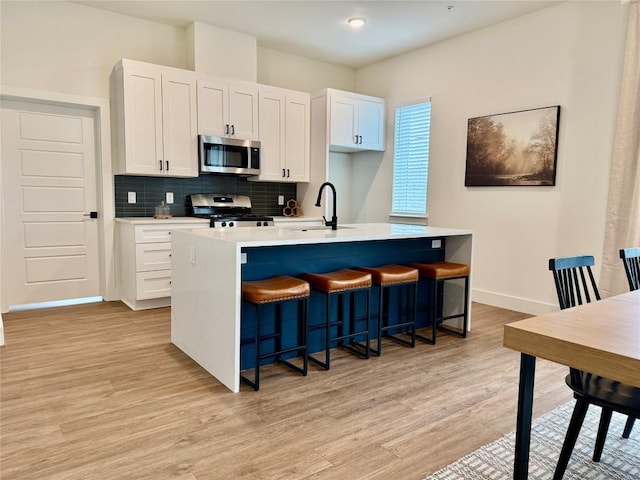 kitchen with a sink, decorative backsplash, light wood-style flooring, appliances with stainless steel finishes, and a kitchen island with sink