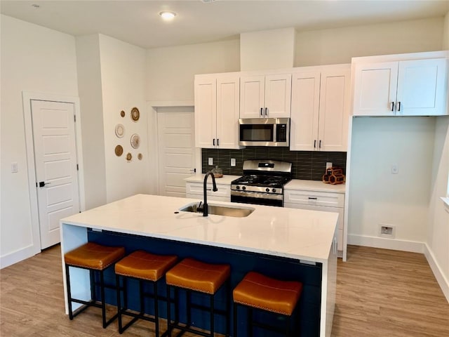 kitchen featuring a breakfast bar, a sink, white cabinets, appliances with stainless steel finishes, and tasteful backsplash