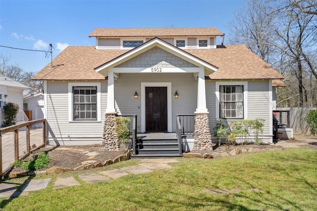 view of front of house featuring a porch, a shingled roof, a front yard, and fence