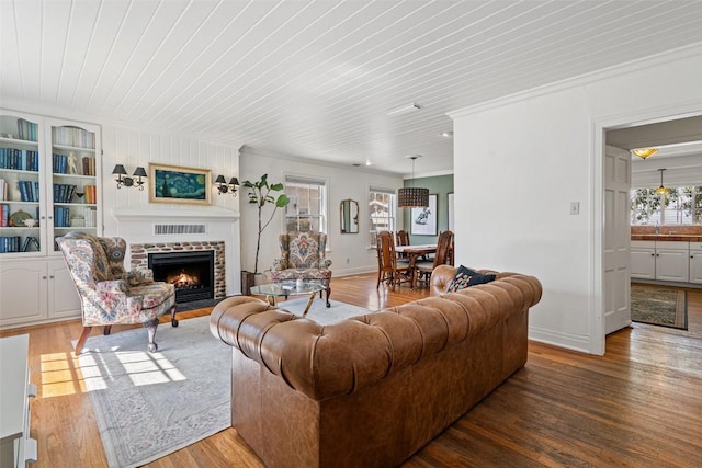 living area featuring baseboards, a fireplace with flush hearth, wood finished floors, and crown molding