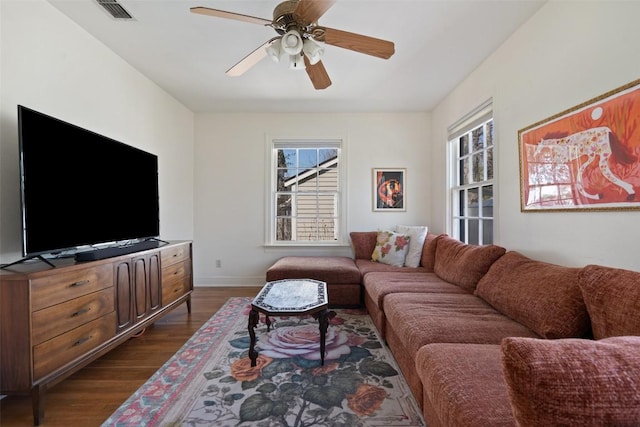 living area with a wealth of natural light, visible vents, ceiling fan, and dark wood-style flooring