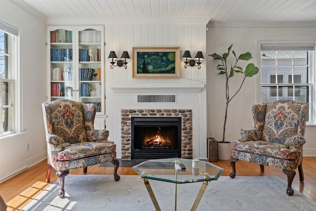 sitting room with wood finished floors, visible vents, a fireplace with flush hearth, wood ceiling, and crown molding