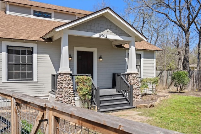 view of front facade featuring a porch, roof with shingles, and fence