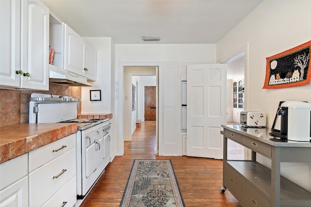 kitchen featuring under cabinet range hood, gas range gas stove, backsplash, dark wood finished floors, and white cabinets