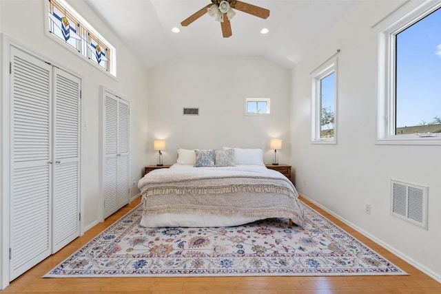 bedroom with lofted ceiling, light wood-style floors, visible vents, and two closets