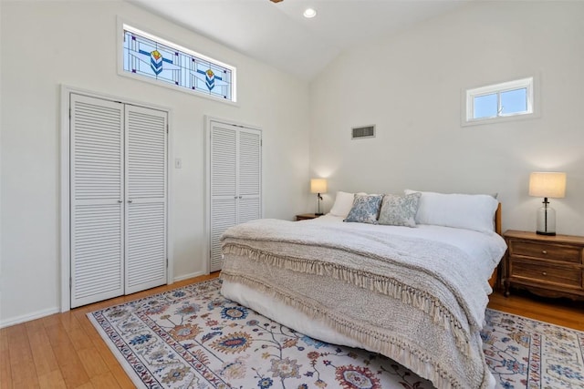 bedroom featuring light wood-style flooring, multiple windows, visible vents, and multiple closets