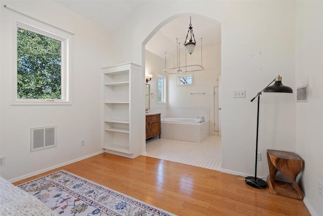 bedroom with arched walkways, visible vents, light wood-type flooring, and baseboards