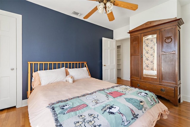 bedroom featuring ceiling fan, visible vents, baseboards, and wood finished floors