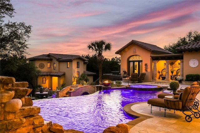 pool at dusk with an outdoor pool, a patio, and an in ground hot tub