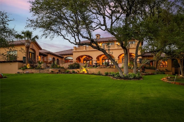 back of property with stucco siding, a tile roof, a yard, a balcony, and a chimney