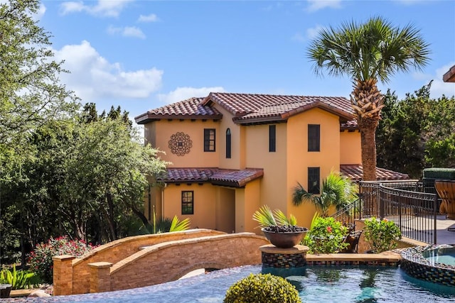 back of house featuring stucco siding, an in ground hot tub, a tile roof, and a fenced in pool