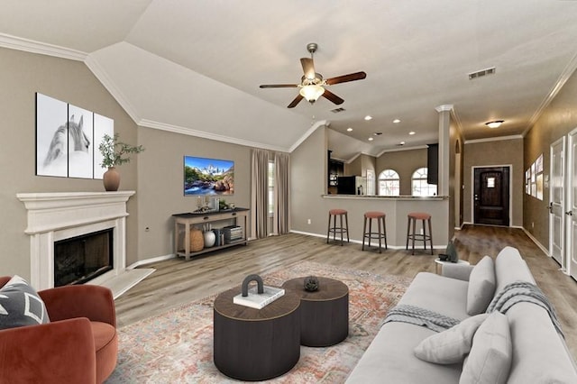 living area featuring visible vents, a fireplace with raised hearth, crown molding, vaulted ceiling, and wood finished floors