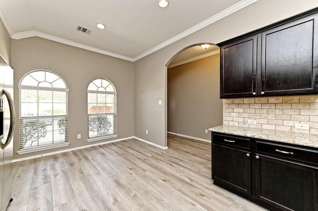 kitchen featuring light stone counters, visible vents, light wood finished floors, baseboards, and arched walkways