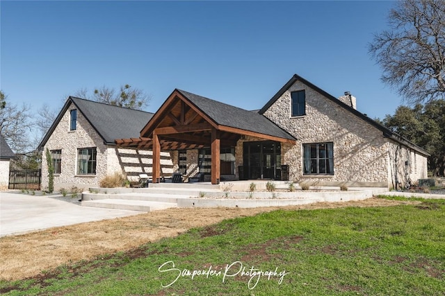 view of front of property featuring stone siding, a front yard, a patio, and a chimney