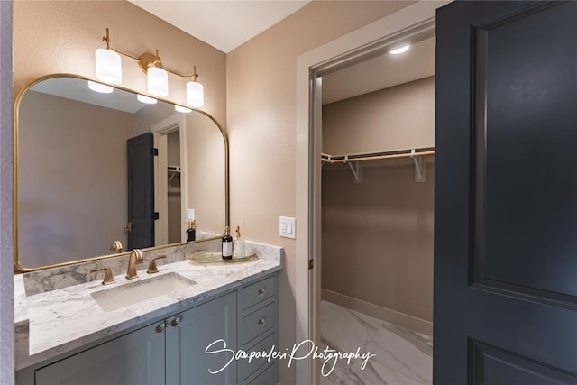 bathroom featuring a walk in closet, baseboards, marble finish floor, and vanity