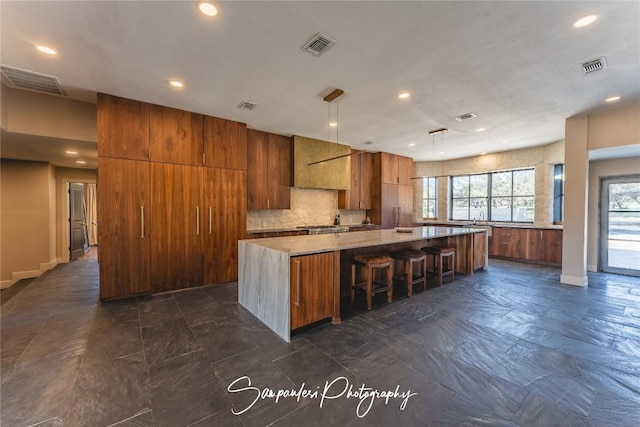 kitchen with a spacious island, visible vents, tasteful backsplash, and brown cabinetry