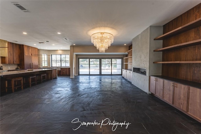 unfurnished living room with a notable chandelier, visible vents, recessed lighting, and stone finish floor