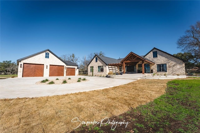 view of front of home featuring stone siding, a garage, concrete driveway, and a front lawn