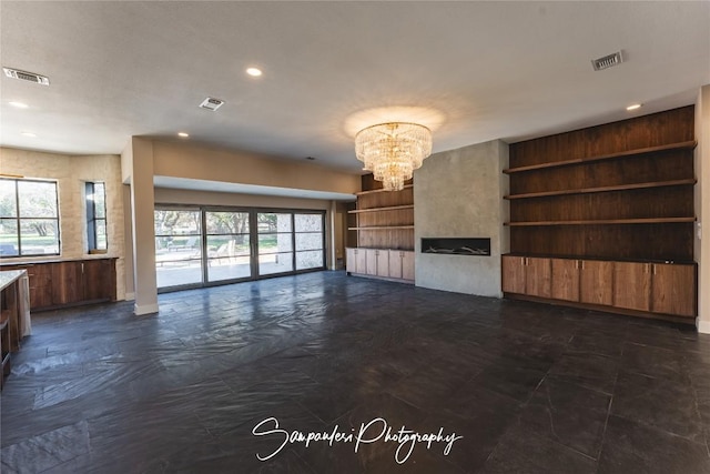 unfurnished living room with built in features, visible vents, and an inviting chandelier