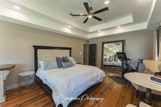 bedroom featuring a raised ceiling, hardwood / wood-style floors, recessed lighting, baseboards, and ceiling fan