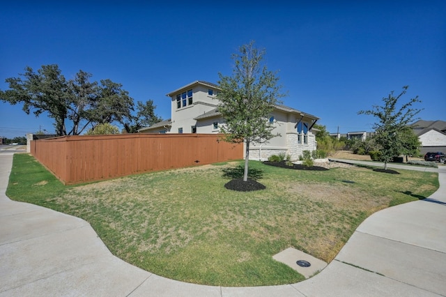 view of side of home with stone siding, a lawn, and fence