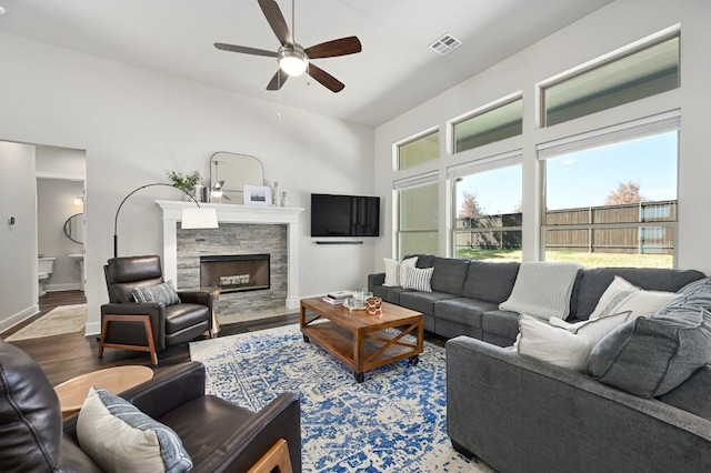 living area with a stone fireplace, wood finished floors, visible vents, and baseboards