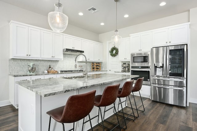 kitchen featuring dark wood-style flooring, stainless steel appliances, white cabinets, under cabinet range hood, and backsplash