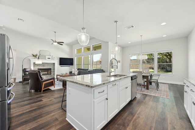 kitchen featuring dark wood finished floors, a fireplace, a sink, appliances with stainless steel finishes, and white cabinetry